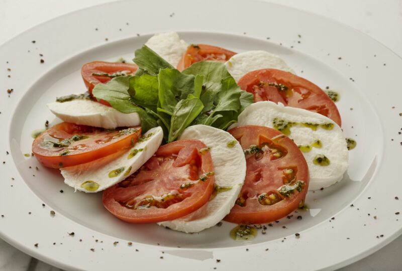 Caprese salad with sliced tomatoes, mozzarella and basil on a white plate